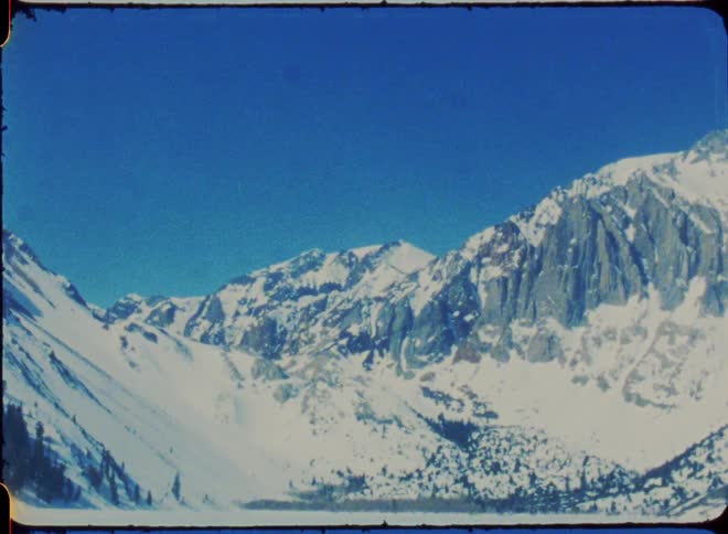 A freezing river sits at the foot of snow covered mountain under a clear blue sky