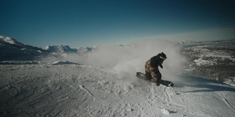 A snowboarder puts his hand in the snow to change direction and avoid going over the edge of the mountain