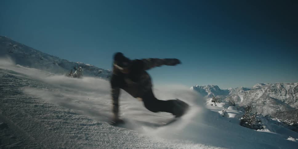 Snowboarding down mountain during the day taking edge and touching snow with hand