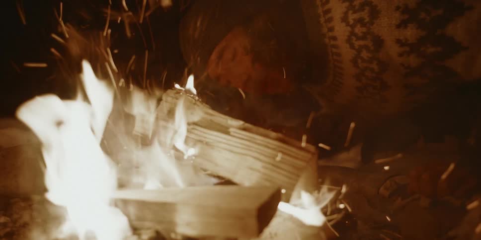 A man blows into a fire to make it grow