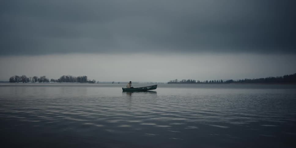 A person sits in a stopped boat in a lake
