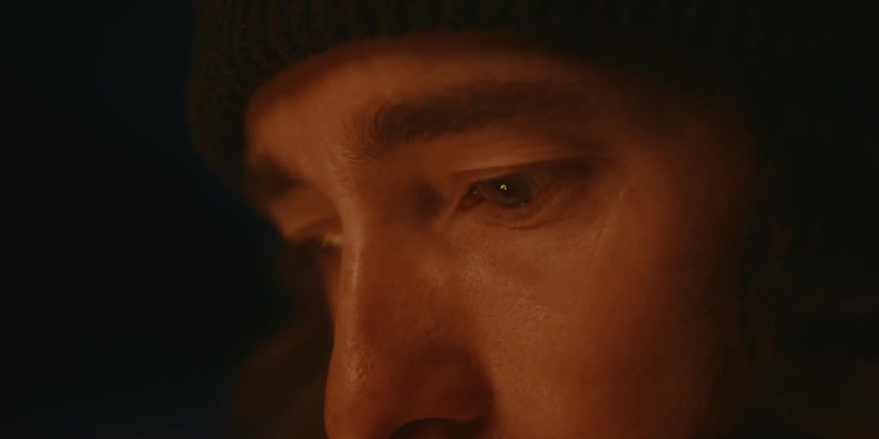 A man wearing a mustache is looking at something with a sad expression