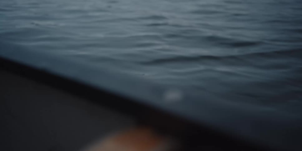 Man sitting in a rowboat in the middle of a lake or the ocean with a thermos of coffee at dawn