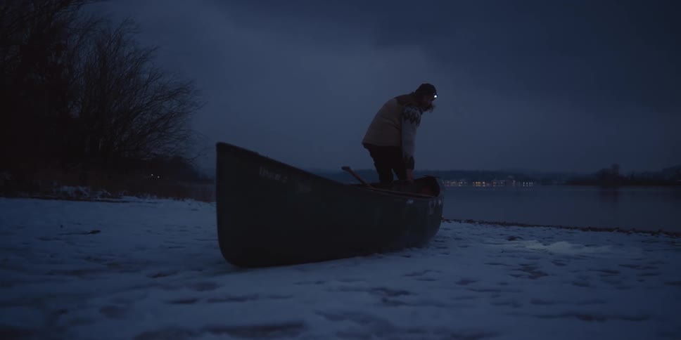 A person drags a canoe through the snow towards a the shoreline of a lake