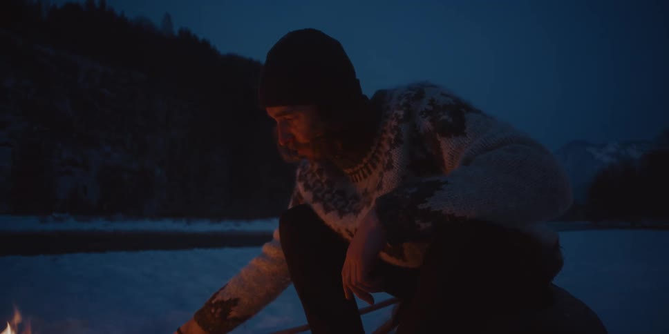 A man concentrates on tending a fire as he sits outside during winter