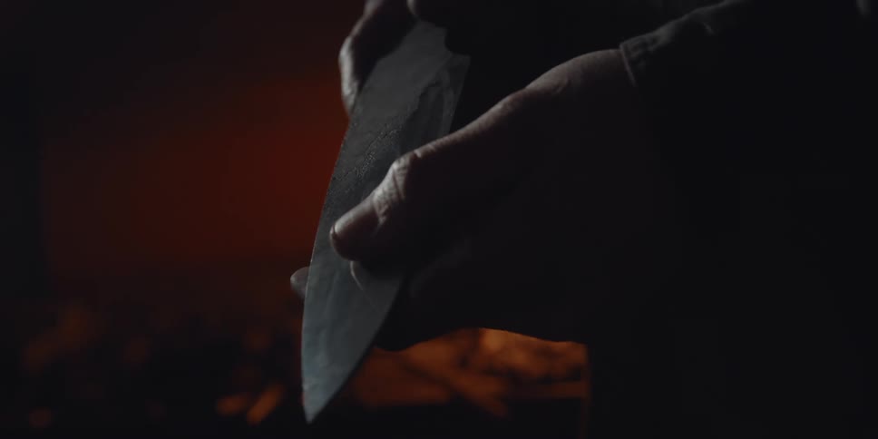 Two hands handle a kitchen knife by a fire