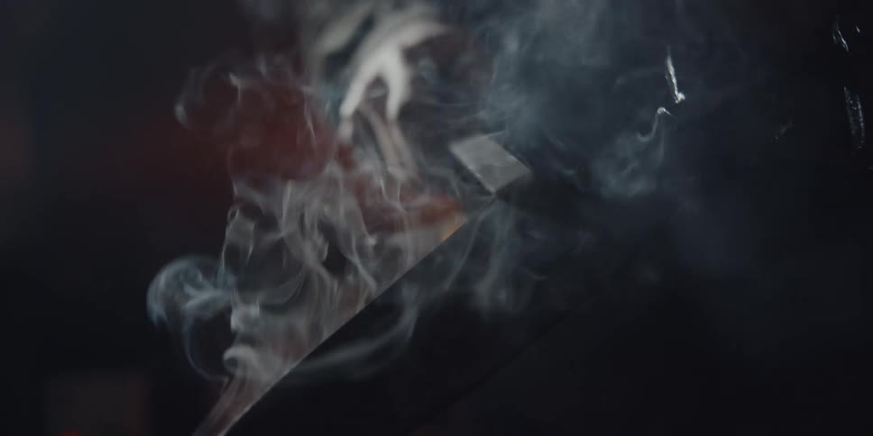 A man sharpens a large knife as it smokes