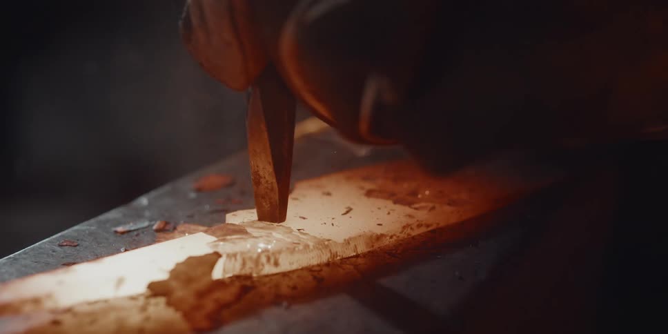 A hammer makes a mark on a piece of blazing hot metal shattering pieces of it