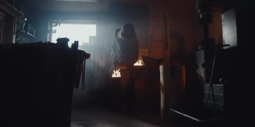 Blacksmith quenches hot blade in oil that results inflames around his gloves