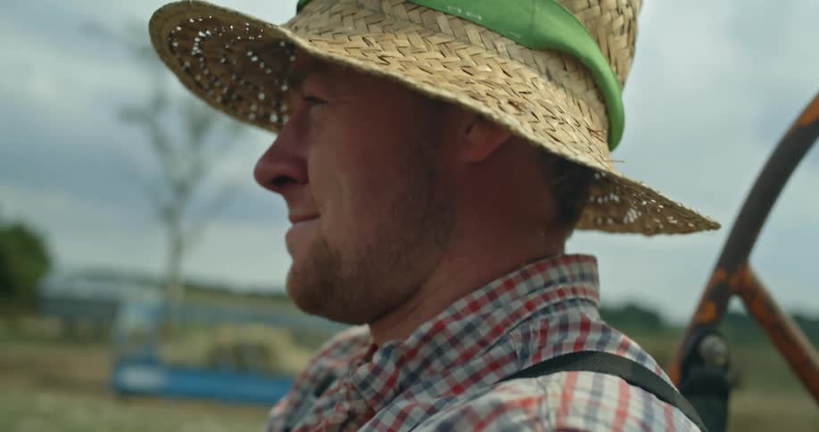 Man with straw hat and plaid shirt drives vehicles on farmland
