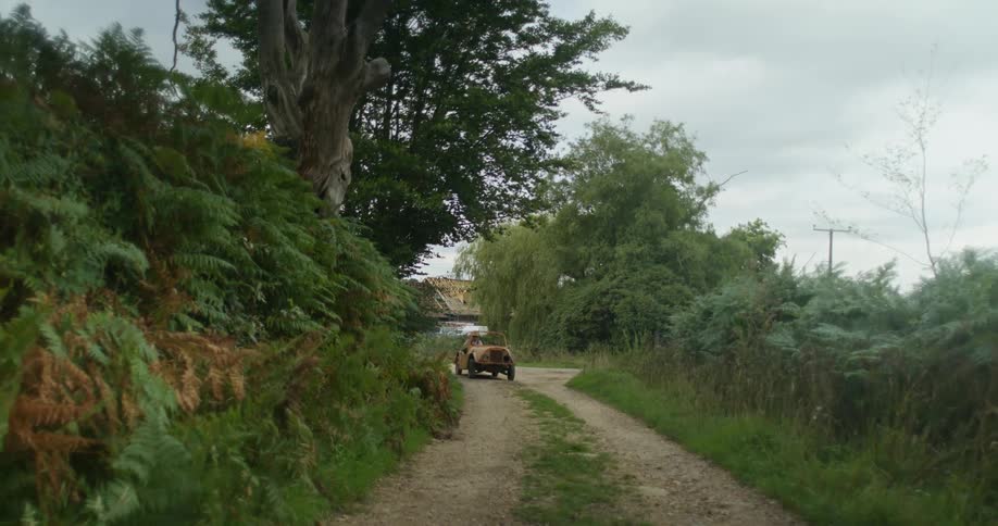 A man comes around a bend in a small vehicle on a rural dirt road