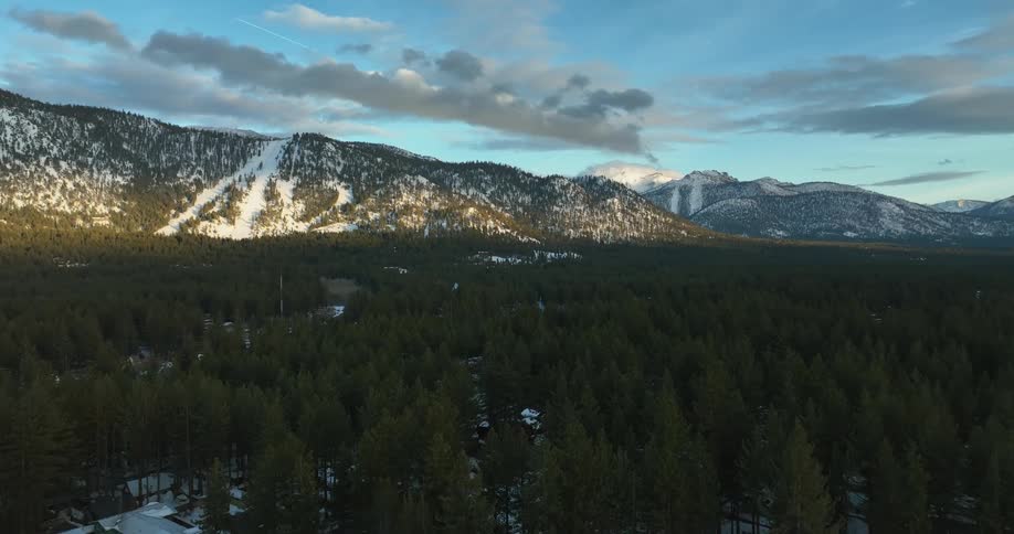 A snow covered mountain ridge looms over a vast forest during the day