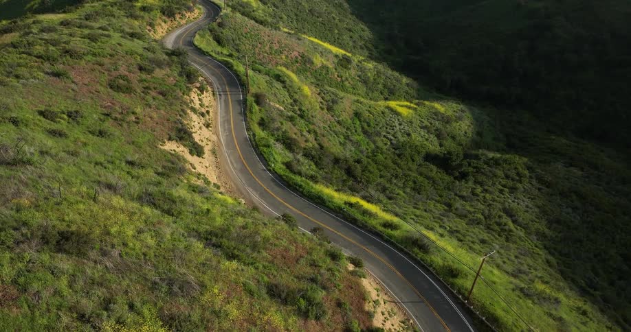 The sun shines upon a crooked mountain road and grass covered hills