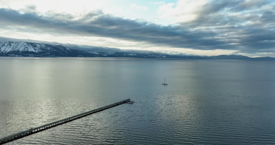 Aerial view of pier and boat sailing off the coast at dusk