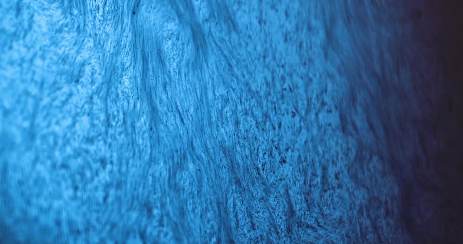 Blue fluid flows down surface containing tendrils and speckles