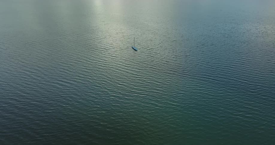 A boat floats in the open water as light shines from above reflecting on the ripples and waves of the ocean