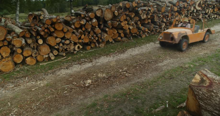 A man drives by a` large stacks of logs
