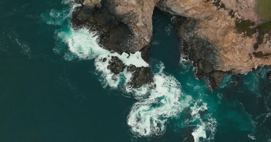 Aerial view of waves crashing beneath rocky cliffs