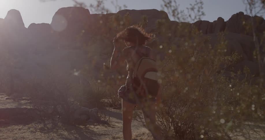 A woman hikes under bright sun in a desert landscape