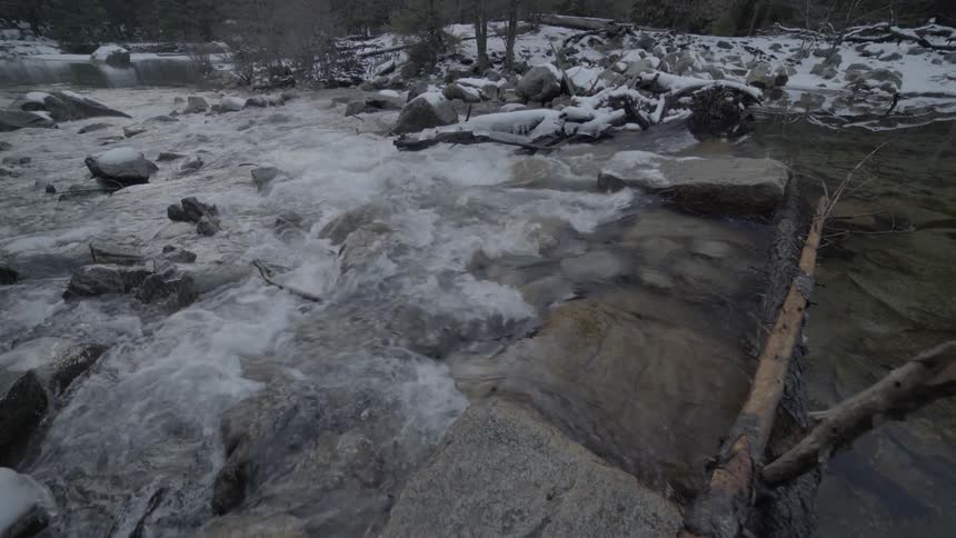 A fast flowing stream moves over rocks in a snowy landscape