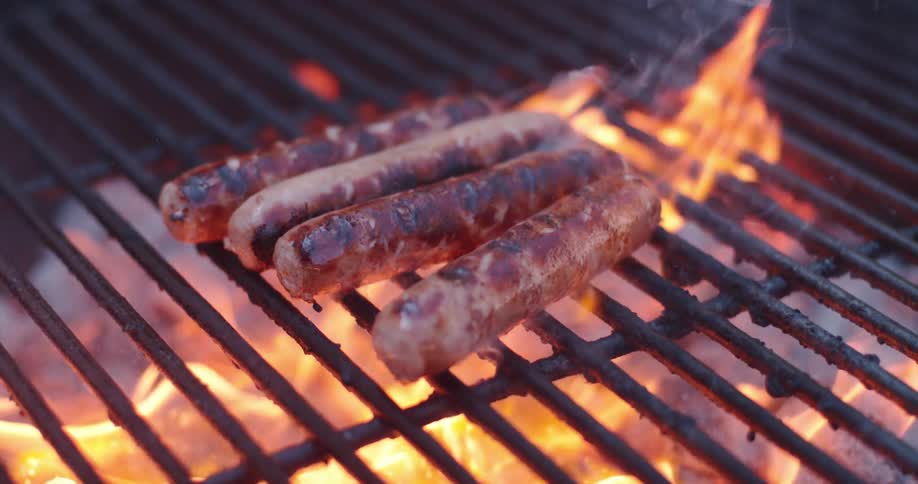 Hot dogs getting charred on a grill