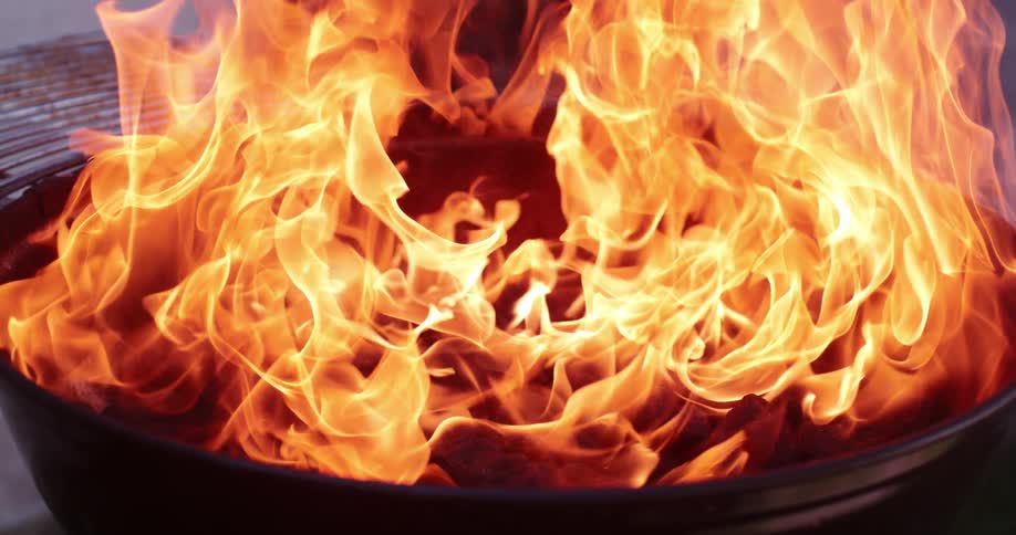 An outdoor grill is filled with a roaring flame outside