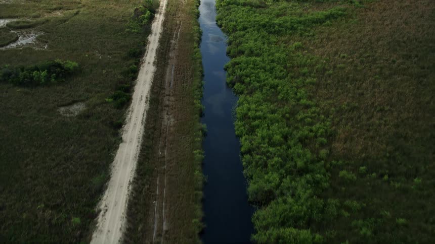 An aerial view of a river meandering alongside a dirt road through lush greenery in Floridas Everglades National Park