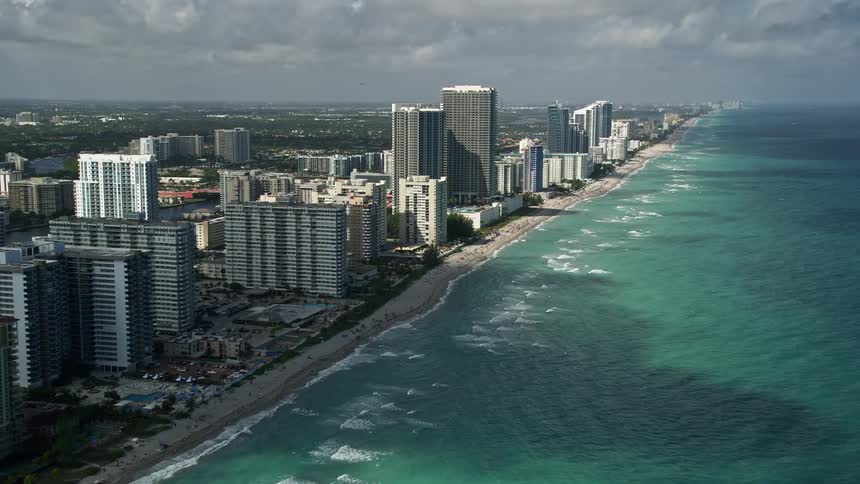 A stunning aerial view of a beach in Hallandale Beach Florida featuring high-rise condominium complexes and sunbathers enjoying the seaside