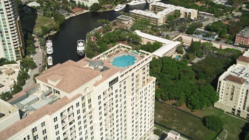 A breathtaking aerial view of a luxurious condominium complex with a rooftop swimming pool located in Downtown Fort Lauderdale Florida surrounded by other towering apartment buildings across a river