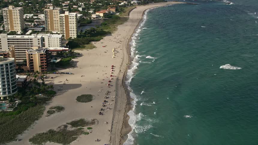 Approaching Hillsboro Inlet Light from above the aerial footage pans down to capture the bustling Pompano Beach coastline and sunbathers