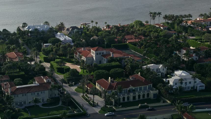 An aerial view of luxurious mansions and residential neighborhoods in Palm Beach Florida with partly cloudy skies and waterfront property