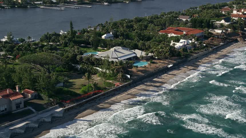 Flying over a coastal mansion with a pool and large home situated in a luxurious neighborhood along the beach in Manalapan Florida