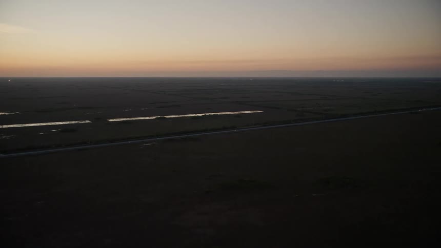 Tracking a car on a two-lane road at twilight in rural Floridas Homestead as wetlands and a country road unfold below