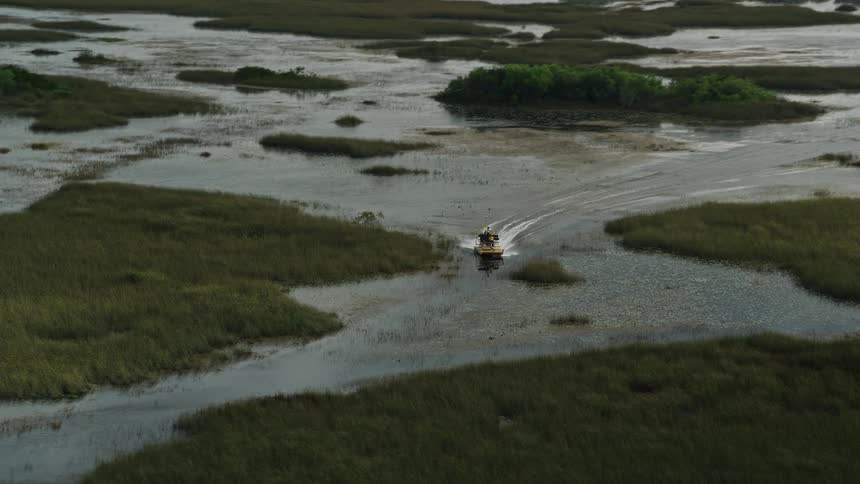 A fanboat races through the marshland of Florida Everglades filmed from an aerial perspective
