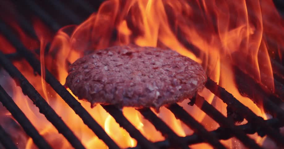 A burger cooking on a grill with flames