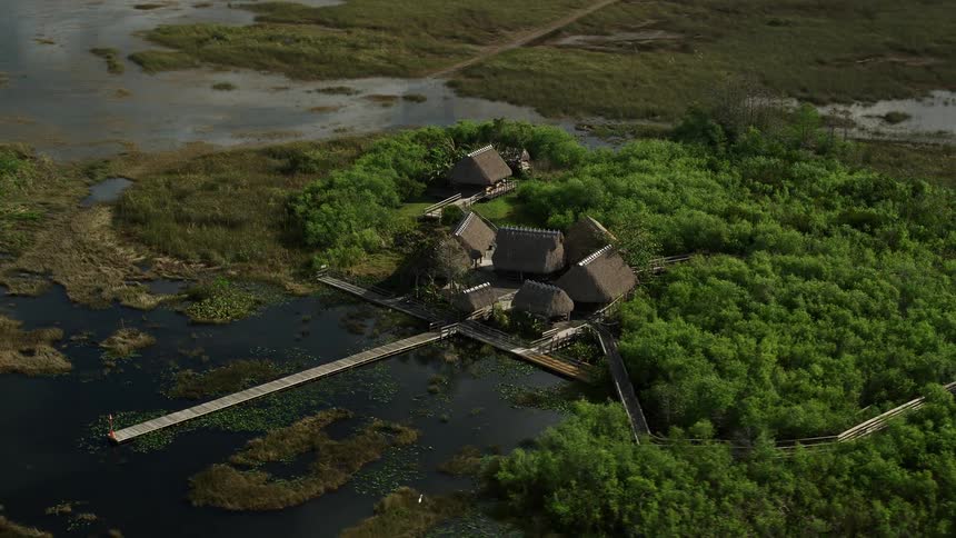 Orbiting aerial view of huts and a dock on marshland in the Florida Everglades providing a natural landmark in partly cloudy skies during daytime
