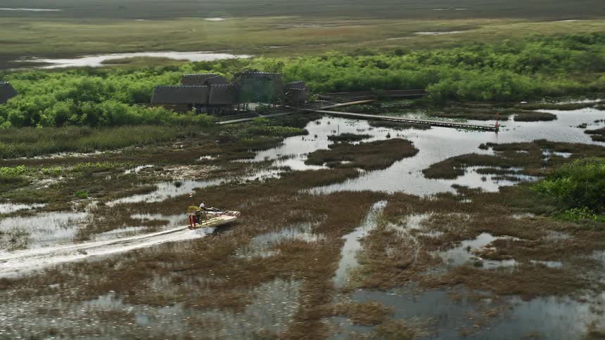An aerial view of a fanboat traveling towards a dock surrounded by marshland in Floridas Everglades