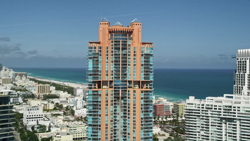 Flying above Miami Beachs South Beach this 5K aerial footage showcases the stunning Portofino Tower and other high-rise buildings boasting impressive architecture amidst the bustling city below
