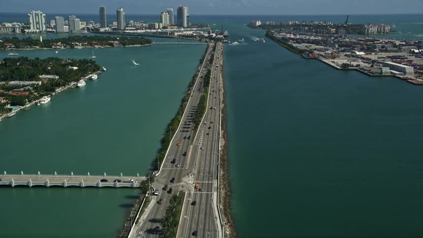 A stunning aerial footage of MacArthur Causeway tilting up and revealing the beautiful South Beach in Miami Florida on a sunny day with light traffic