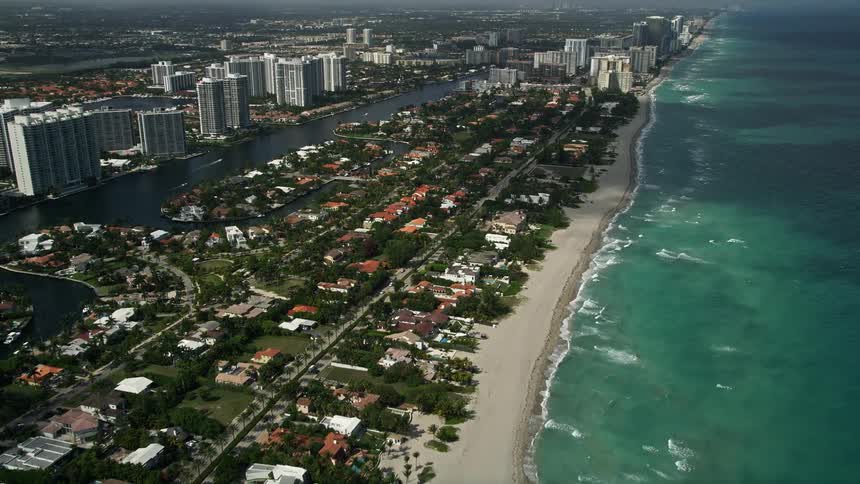 Approaching aerial view of a sunny and upscale residential neighborhood on the shore of Golden Beach Florida