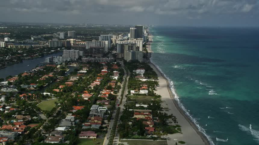 An aerial view of residential buildings and coastline approaching Hallandale Beach and Golden Beach south Florida on a partly cloudy day