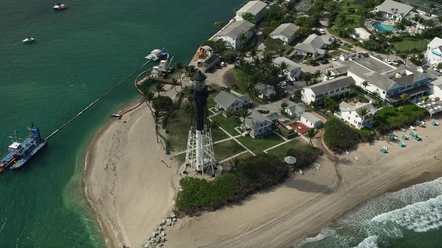 An aerial view of Hillsboro Inlet Light a famous black and white lighthouse on the sunny Florida coast surrounded by beachgoers and shoreline homes