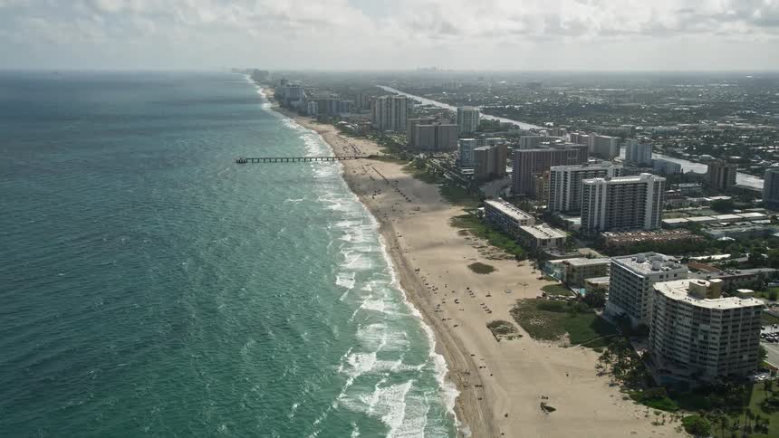 A breathtaking aerial view of Pompano Beach Florida approaching Pompano Beach Pier showcasing the beautiful coastline and beachgoers basking in the sunshine
