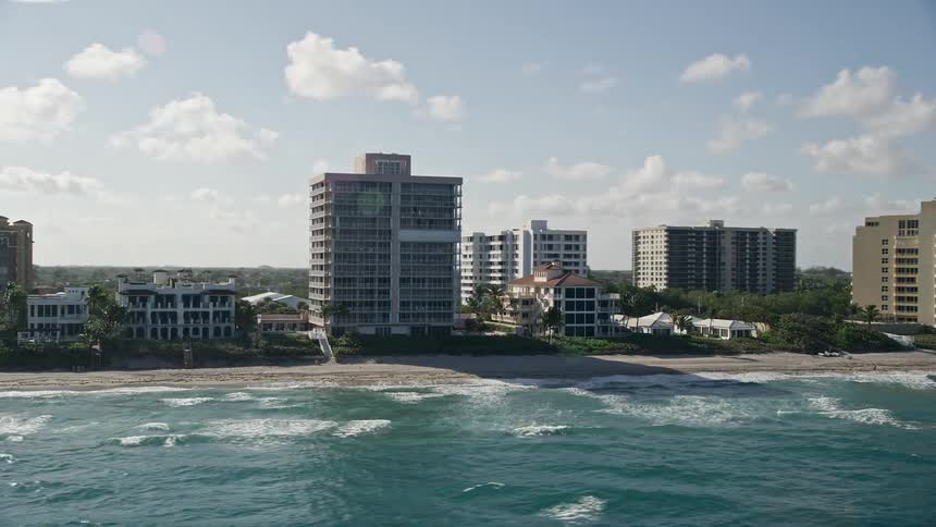 An aerial view of an apartment building-lined beachfront in Highland Beach Florida with partially cloudy skies and some beachgoers visible