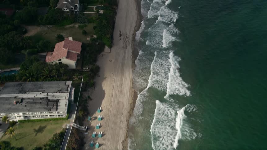 Aerial view of homes along the beach in Hillsboro Beach Florida on a partly cloudy day with crashing waves and beachgoers