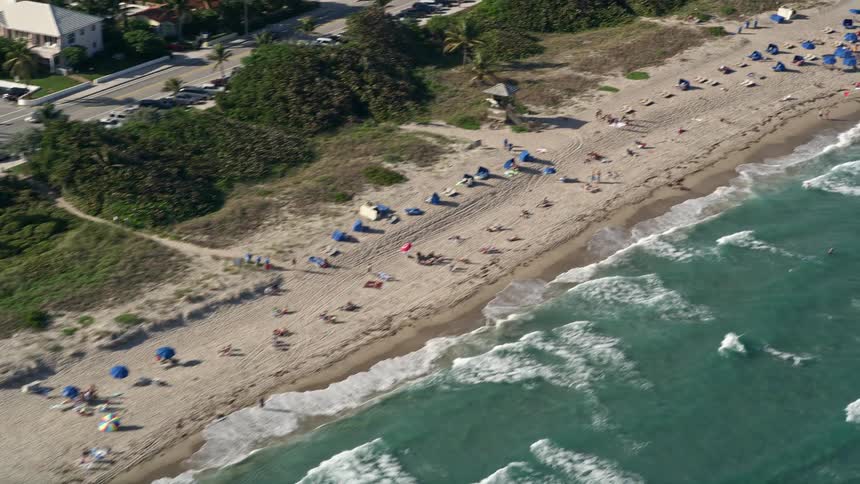 Aerial footage of sunbathers enjoying a sunny day on Delray Beach Florida with waves rolling in and beachgoers lining the shoreline