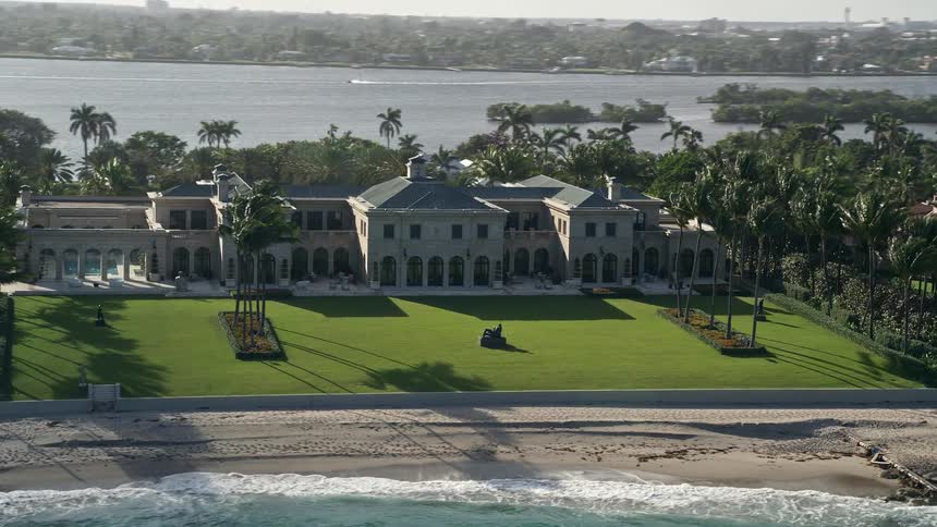 Aerial view of a mansion with palm trees and a sandy beach in front located in Palm Beach County Florida