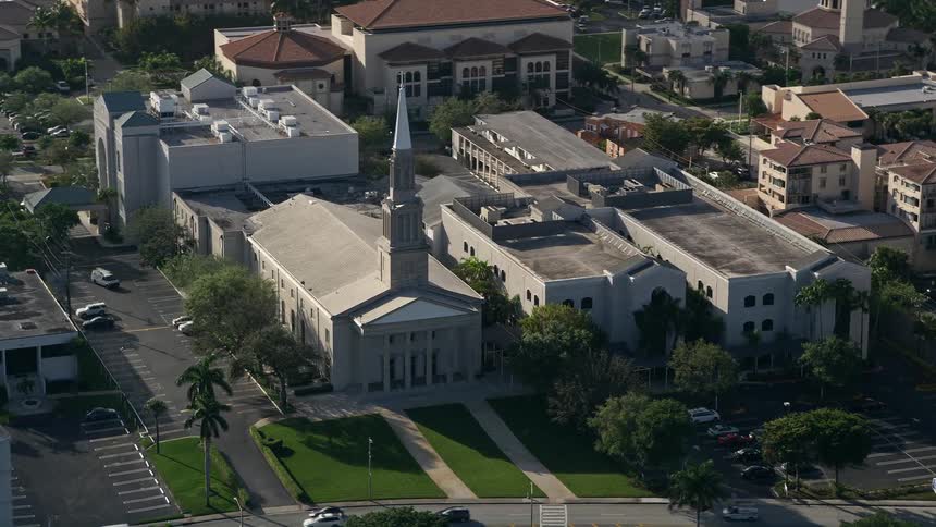 An aerial shot of the First Baptist Church Palm Beach in West Palm Beach Florida surrounded by nearby apartment buildings filmed during a partly cloudy summer day