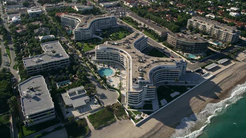 Approaching a uniquely-shaped beachfront condominium complex with a small round pool in the courtyard in Palm Beach Florida during summer