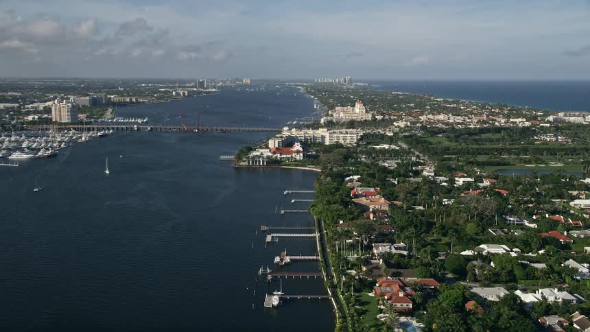 Aerial footage of the Flagler Memorial Bridge and Henry Morrison Flagler Museum in Palm Beach Florida overlooking the Intracoastal Waterway and the coastal community on a partly cloudy day during spring or summer